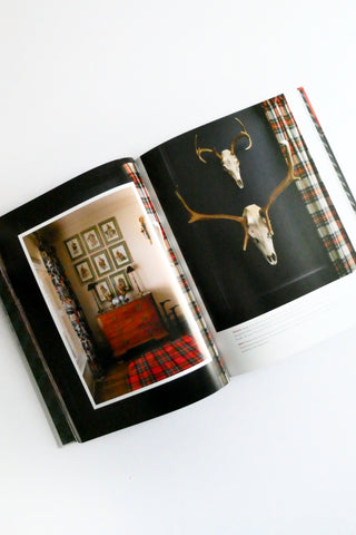 Open book showing a page with a deer skull and another with framed pictures on a wall.