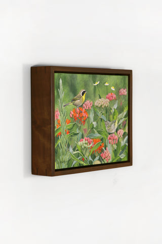 Framed artwork of a bird among flowers on a white wall