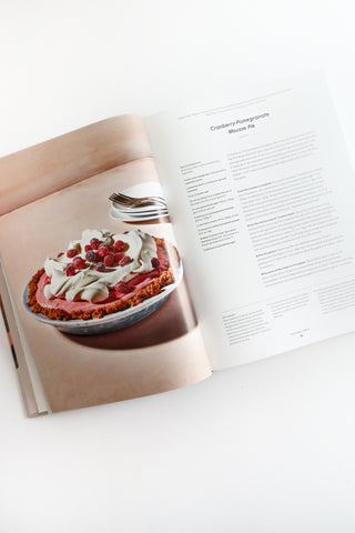 Open cookbook showing a dessert with berries and cream on a white surface