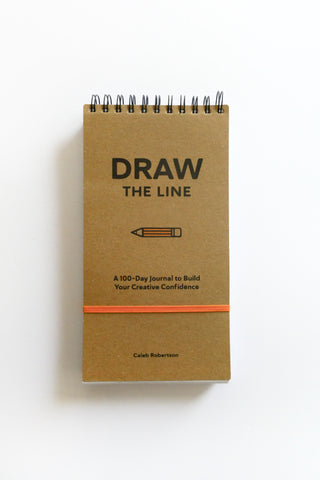 Brown notebook with 'Draw The Line' text on a white background