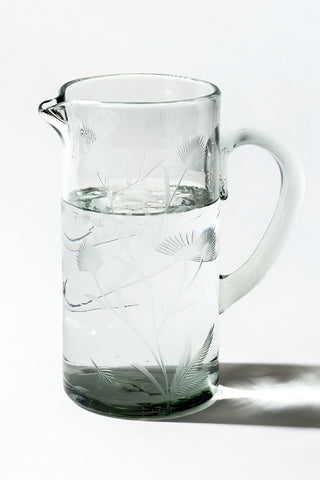 Clear glass pitcher with floral etching on a white background