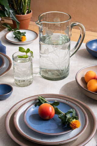 Table setting with ceramic plates, a glass pitcher, and fruits on a light surface.