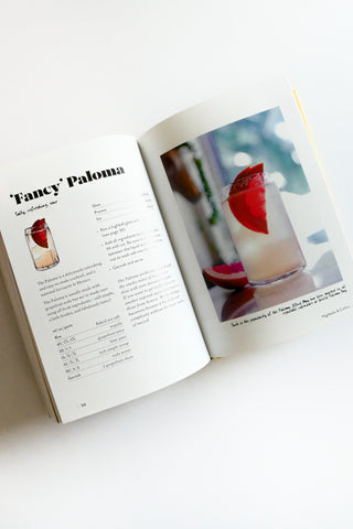 Open book showing a cocktail recipe for 'Fancy Paloma' with a photograph of a cocktail on a white surface.