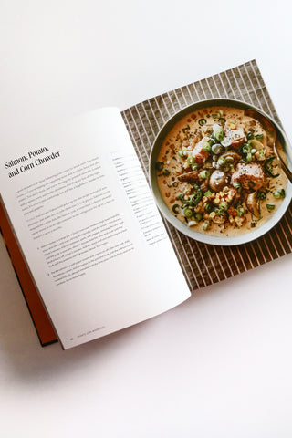Open cookbook showing a recipe for Salmon, Potato, and Corn Chowder on a white surface.