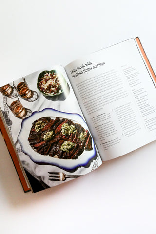 Open cookbook showing a recipe for steak with scallion butter and sake on a white surface.