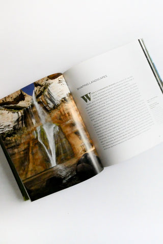 Open book with a page showing a waterfall and another with text on a white surface