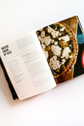 Open cookbook showing a recipe for 'White Shade of Kale' pizza with a photograph of a dish on a white background.