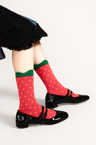Red polka dot socks with green trim worn with black shoes on a white background