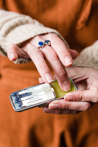 Person holding a tin of scented balm with a blurred background