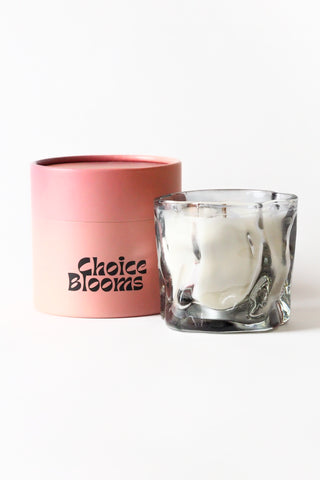 Glass candle in a clear holder with a pink container labeled 'Choice Blooms' on a white background